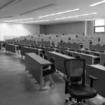 Black and white photo of an empty university lecture hall with rows of desks and chairs