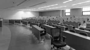 Black and white photo of an empty university lecture hall with rows of desks and chairs