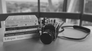 Black and white photo of a vintage camera next to a stack of books on psychology, leadership and longevity.