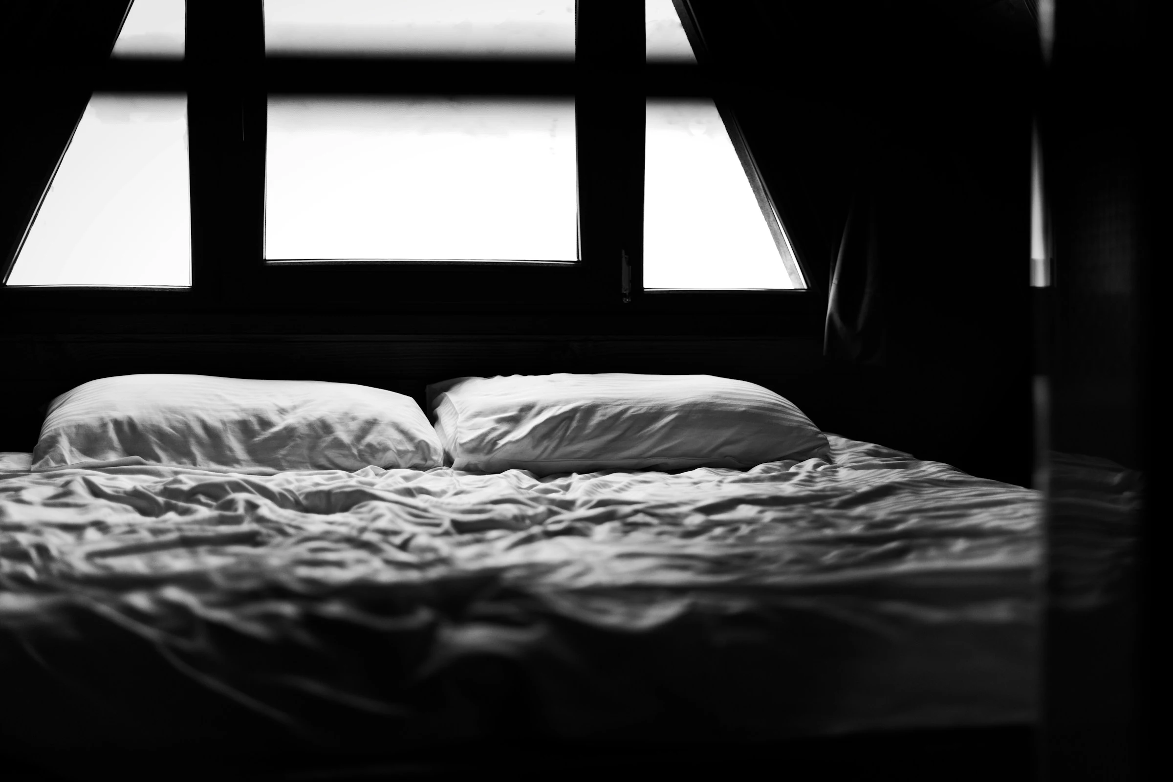 Unmade bed with two pillows in soft morning light coming through a window, symbolising rest and exhaustion after a night shift.
